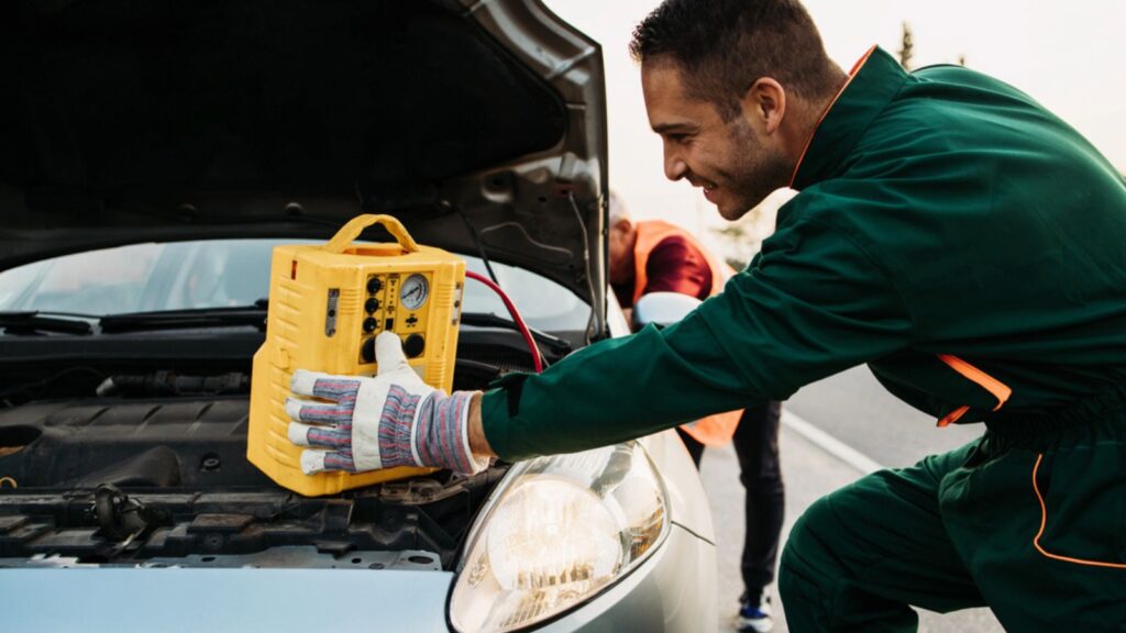 Two road assistant workers in towing service trying to start car engine with jump starter and energy station with air compressor. Roadside assistance concept
