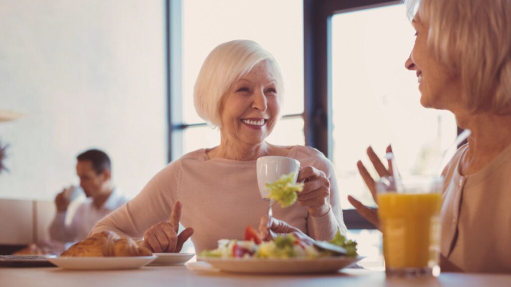 Two upbeat elderly women talking in cafe