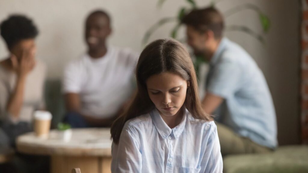 Upset bullied young girl sitting alone excluded by bad friends