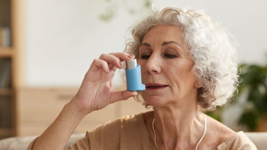 Warm toned head and shoulders portrait portrait of senior woman using inhaler for asthma or breathing problems in home setting