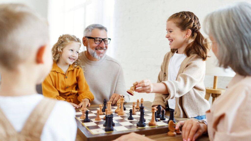 children brother and sister playing chess game with grandparents old retired family