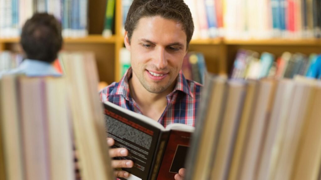happy educated smart man reading book in library research history study