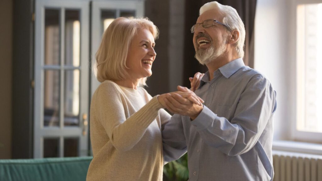 happy retired old couple dancing at home celebrating laughing