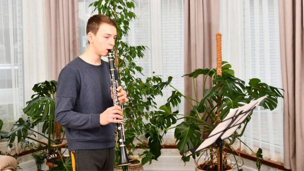 A young guy plays the clarinet from notes. Learning music at home