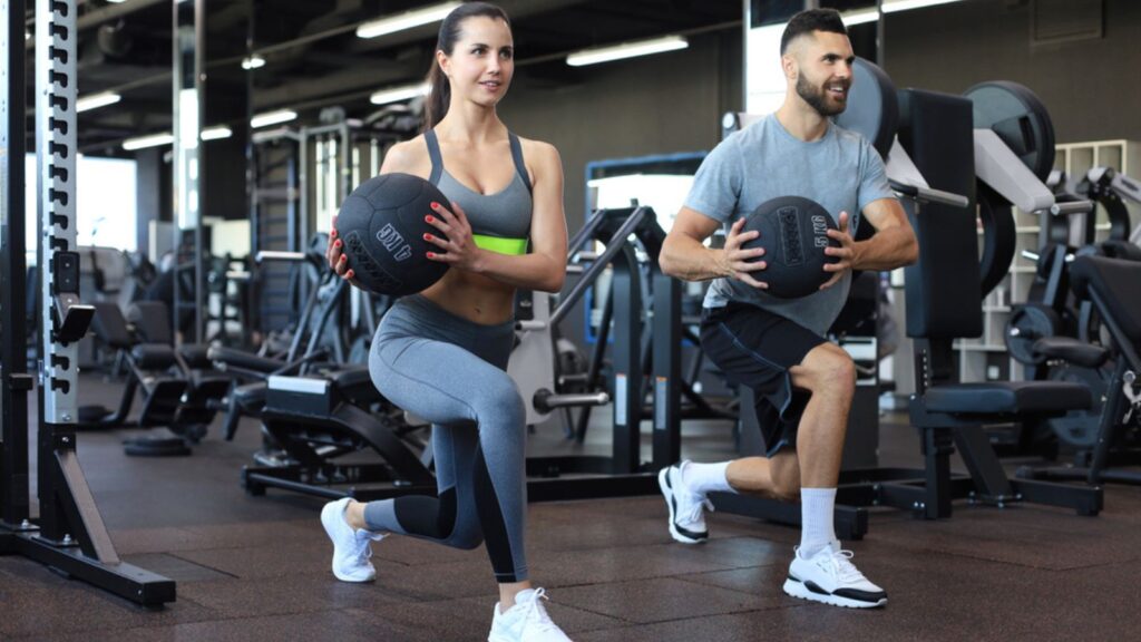 Beautiful young sports couple is working out with medicine ball in gym