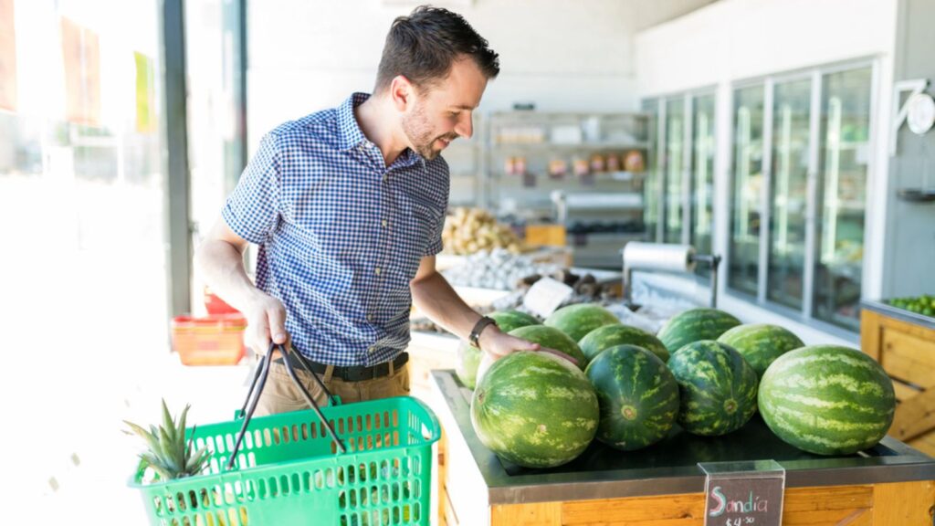Caucasian man carrying shopping basket while buying watermelon from supermarket