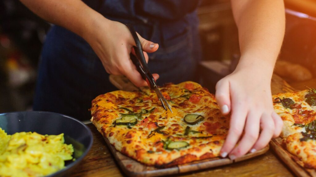 Chef hands cuts pizza with kitchen scissors