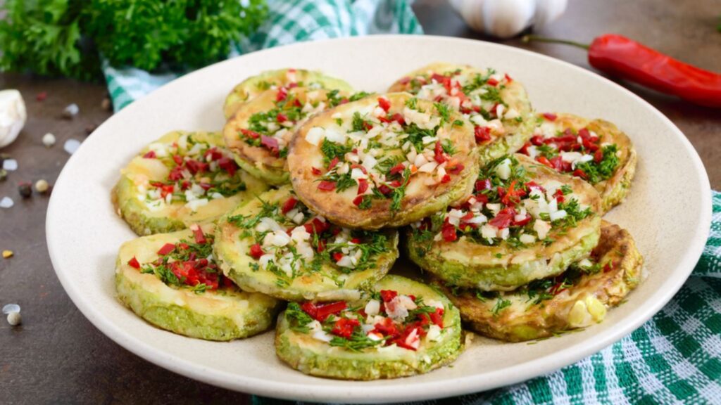 Fried circles of young zucchini with garlic, red pepper, greens on a plate. Vegetarian menu. Close up