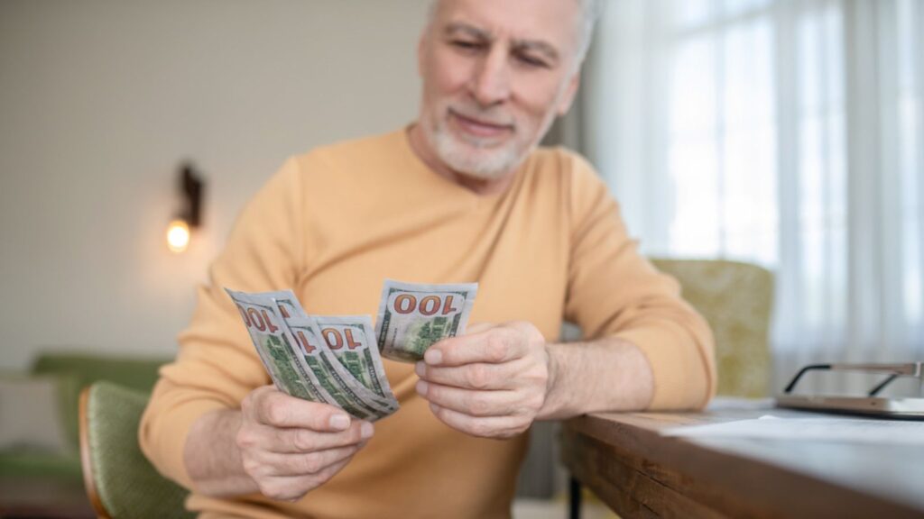 Gray-haired senior man standing and counting money