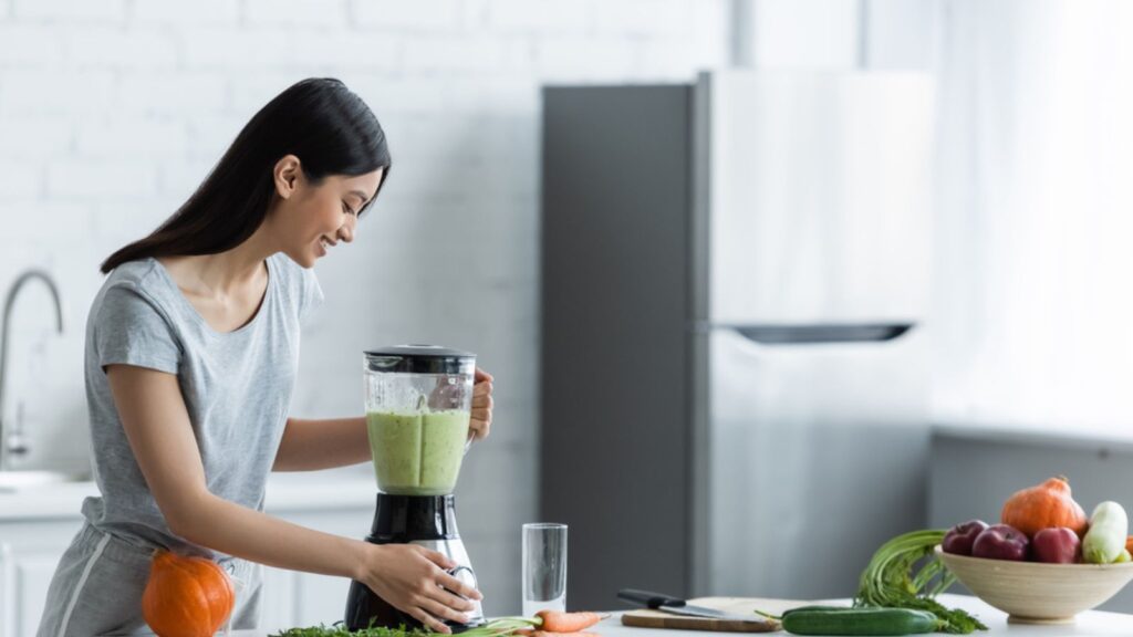 Happy asian woman preparing fresh smoothie for breakfast in kitchen