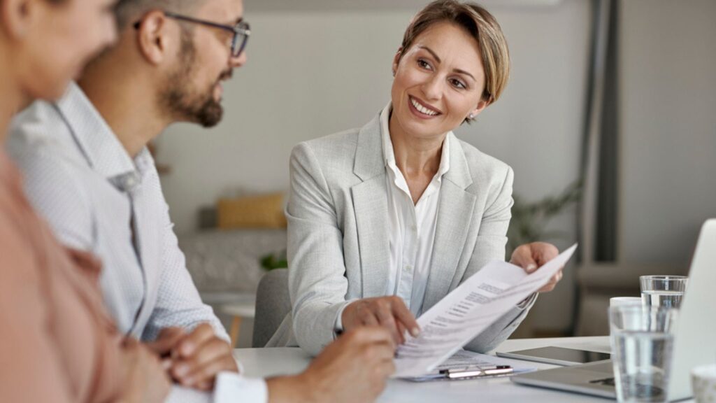 Happy insurance agent talking to a couple and offering them to sign a contract during a meeting