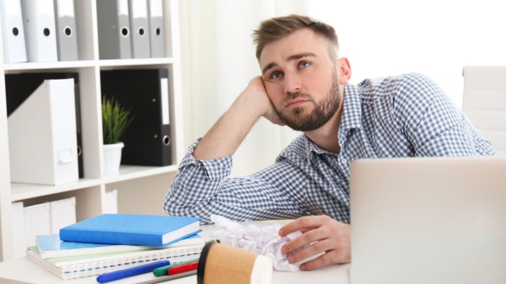 Lazy young man wasting time at messy table in office