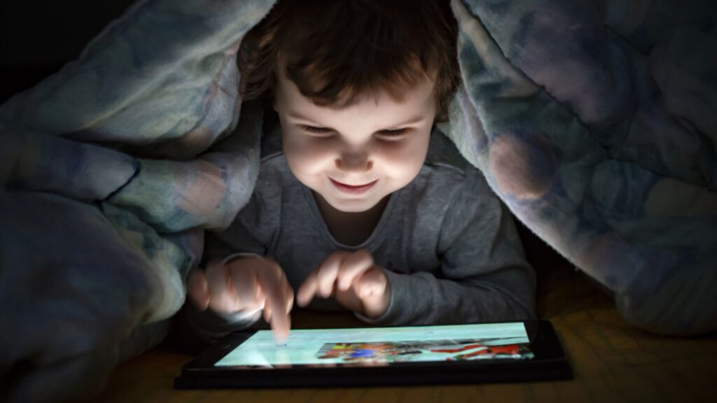 Little girl watching her tablet in the bed at night