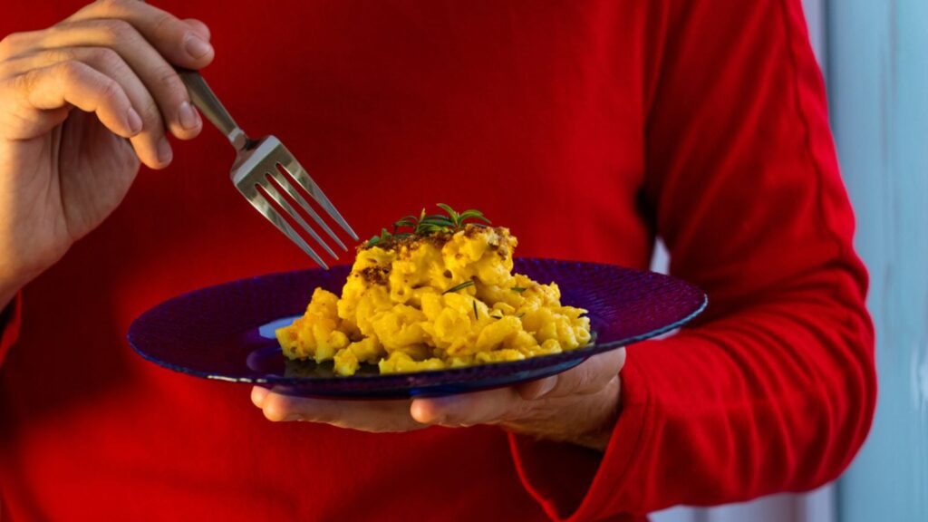 Mac and cheese, baked macaroni pasta cheesy creamy milk butter sauce american style with breadcrumbs crust. Hot casserole on blue plate in male chef hands