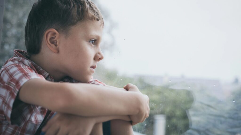 Portrait one sad little boy sitting near a window at the day time