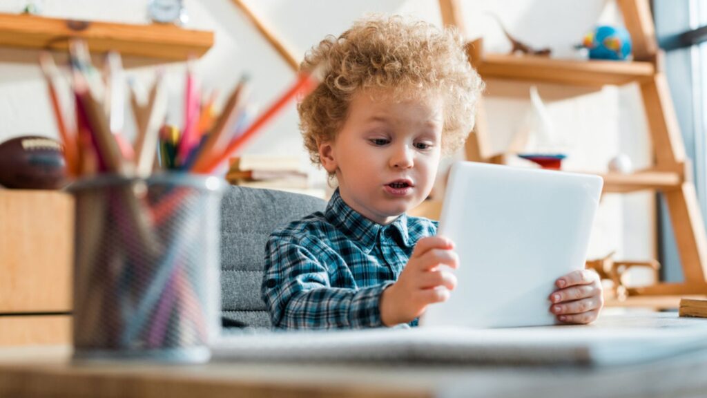 Selective focus of cute curly boy using digital tablet