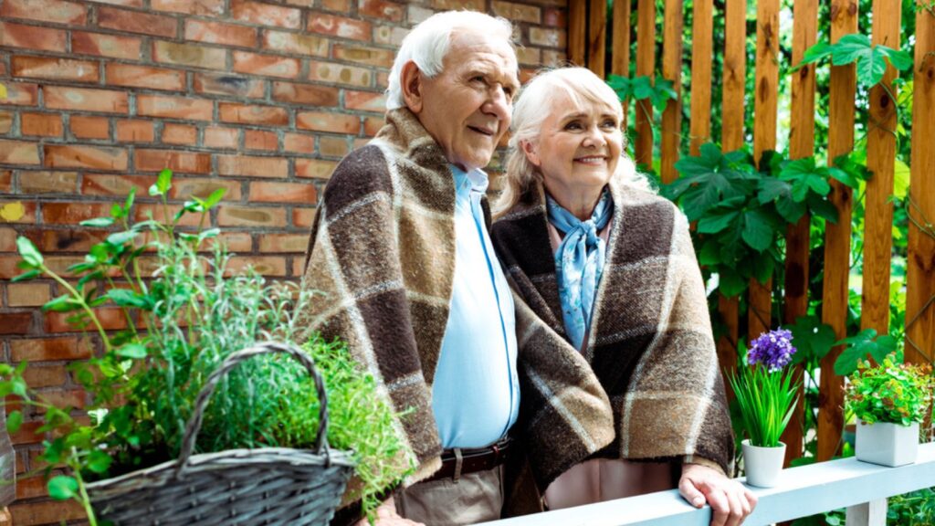 Selective focus of happy senior wife and husband standing in plaid blankets near plants