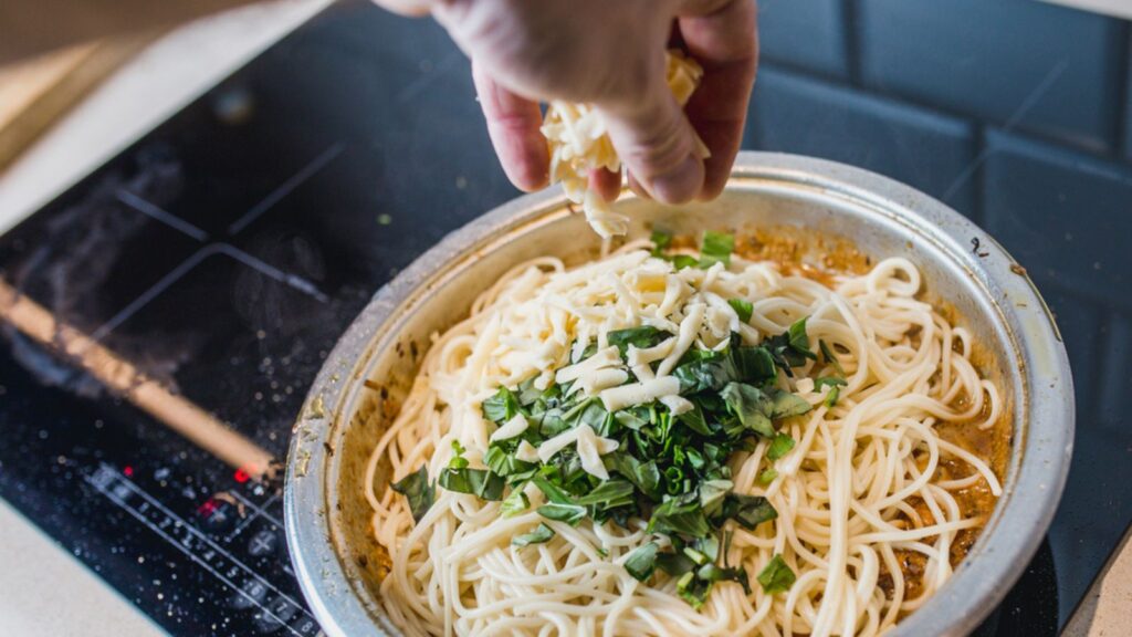Spaghetti pasta in a creamy sauce in a frying pan with chopped basil, cheese and spices - cooking at home