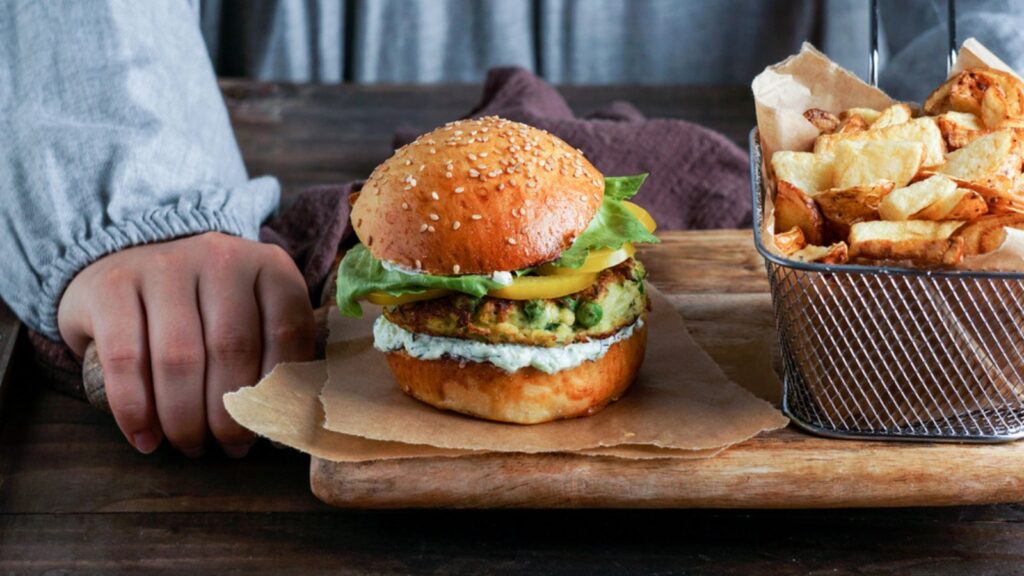 Vegan lentil burgers in the womam hands, with salad and yogurt sauce on a white background. Plant based food concept