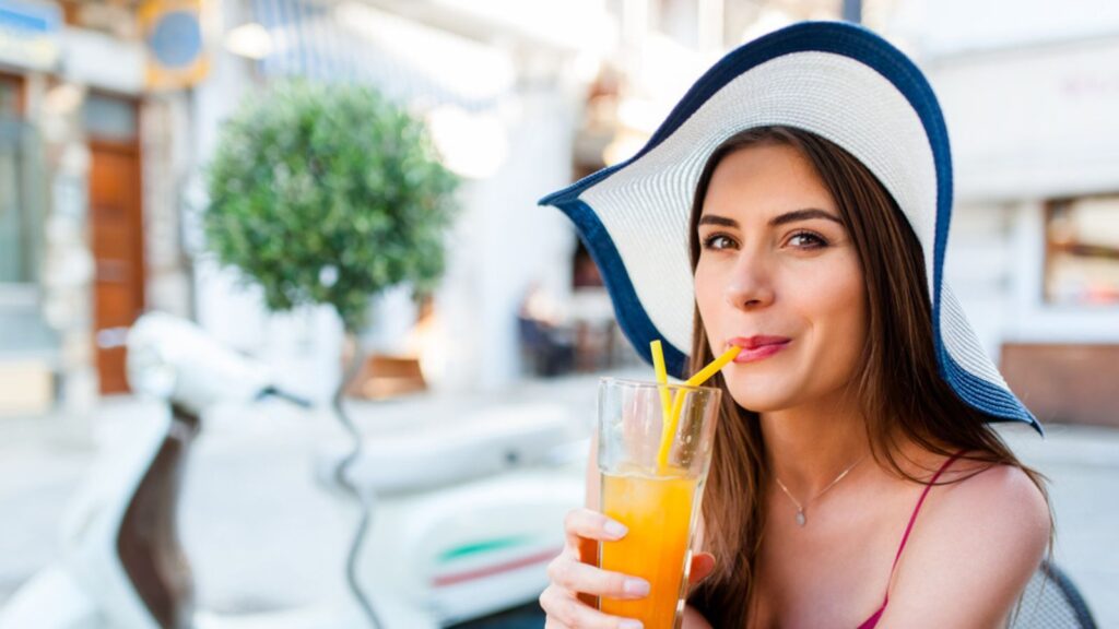 Woman at street terrace in greek village on a hot summer day drinking a orange juice. Summer mediterranean vibe, travel and leisure concept.