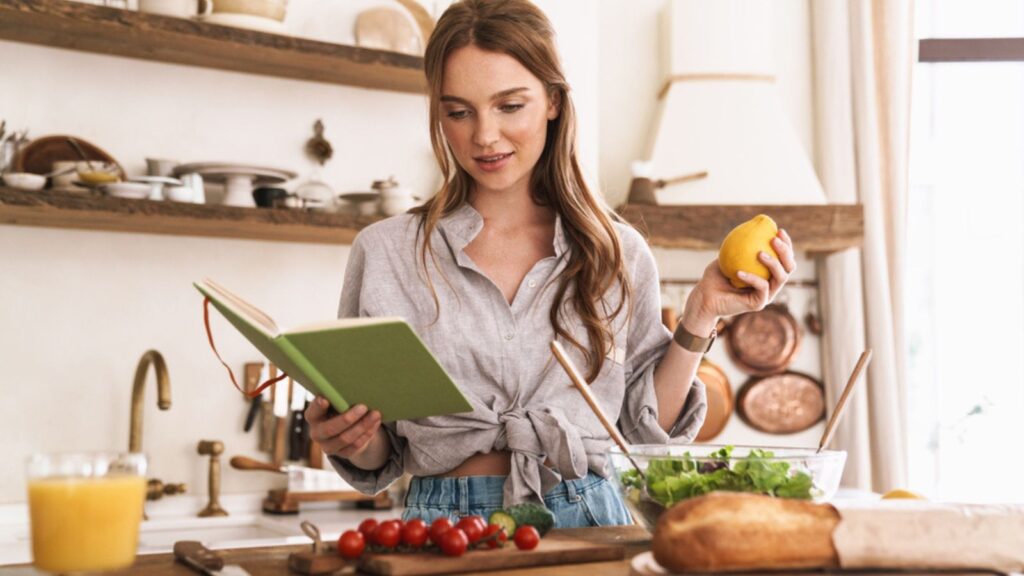 Woman indoors at the kitchen cooking holding notebook and lemon