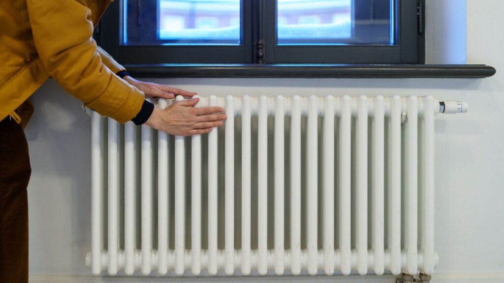 Woman warming hands near heating radiator after winter walk, female checking battery temperature