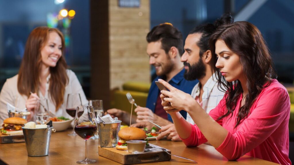 Woman with smartphone and friends at restaurant. No table manners