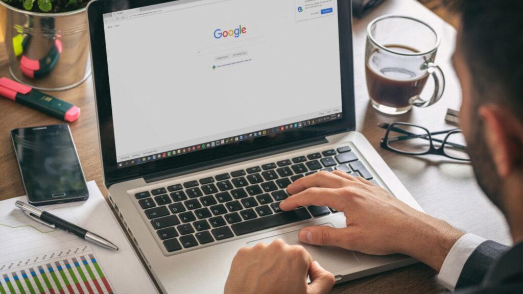 Young man working with a laptop, Google search engine on the computer screen, office workspace
