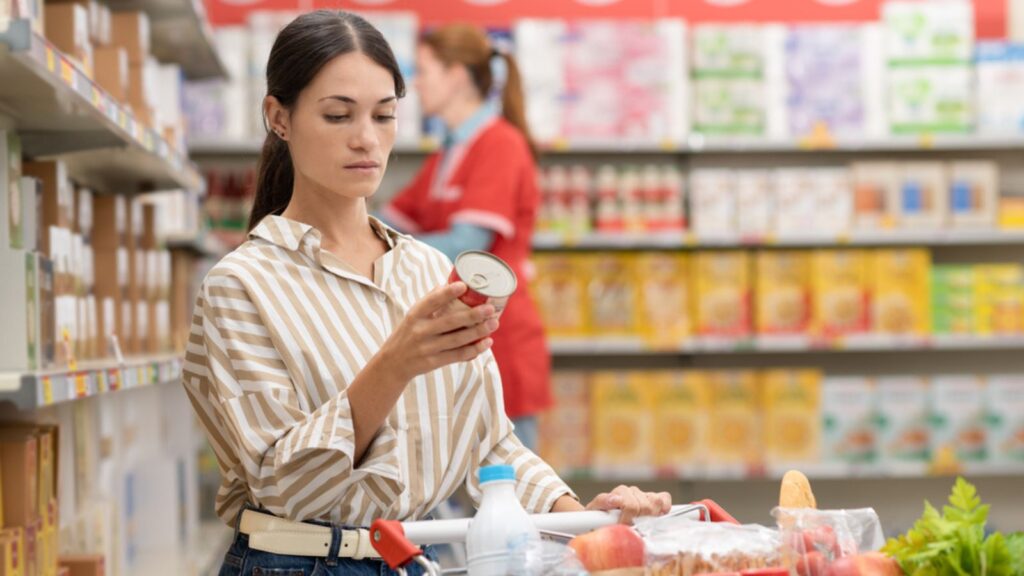 woman grocery store shopping holding can in aisle thinking food