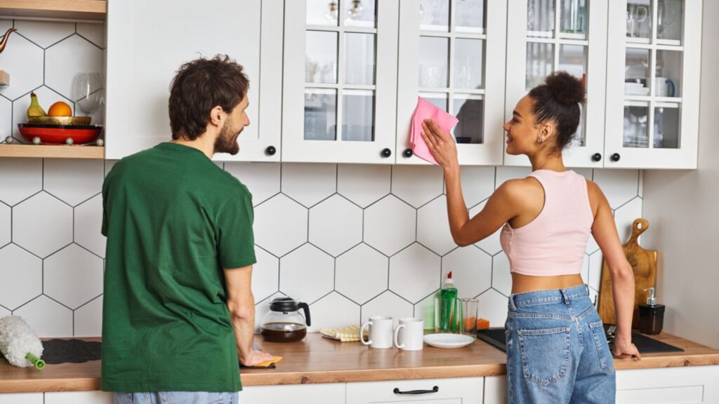 Appealing interracial jolly couple in casual outfits washing surfaces in kitchen, spring cleaning