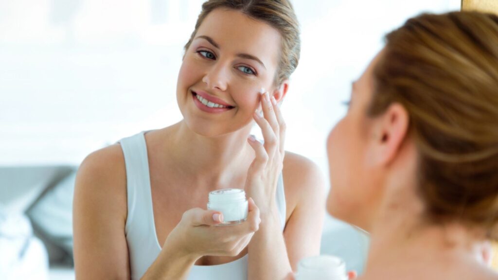 Beautiful young woman caring of her skin standing near mirror in the bathroom