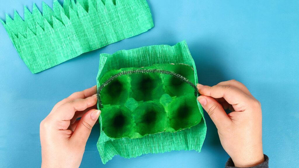 DIY basket Easter egg from cardboard tray, crepe paper, chenille stem on blue background. Gift idea, decor spring, Easter. Handmade. Step by step. Children Easter craft