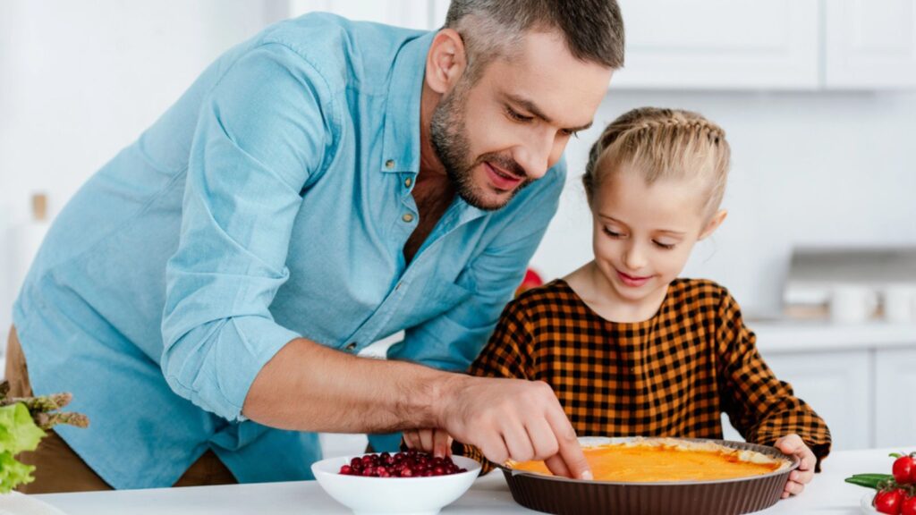 Happy father and adorable little daughter decorating pumpkin pie for thanksgiving day