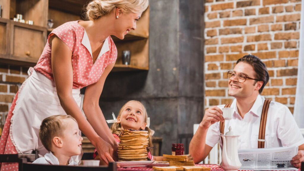 Happy mother holding pancakes for breakfast and looking at husband and kids, retro styled