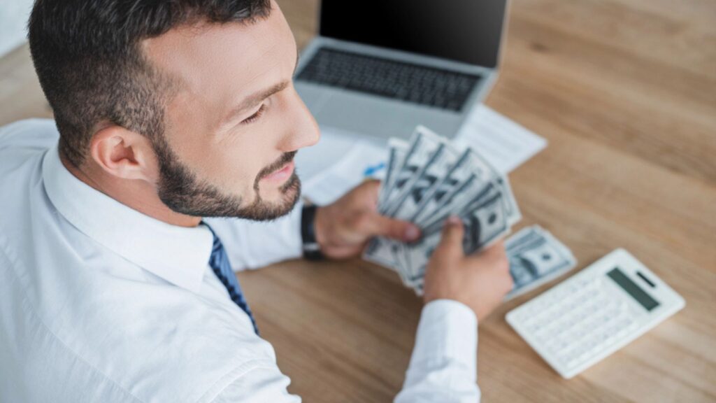 High angle view of financier counting cash with calculator in office