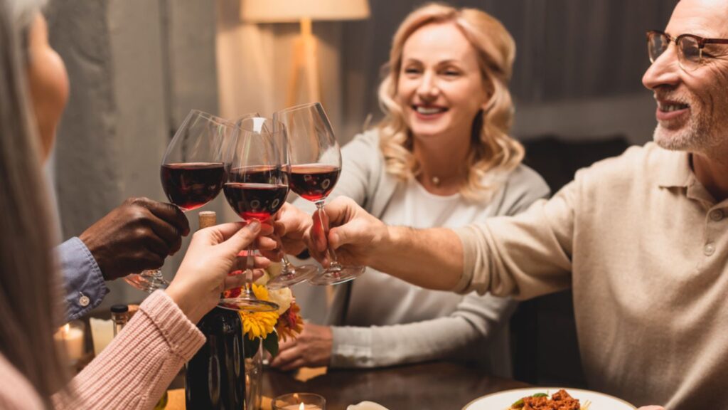 Selective focus of smiling multicultural friends drinking during dinner