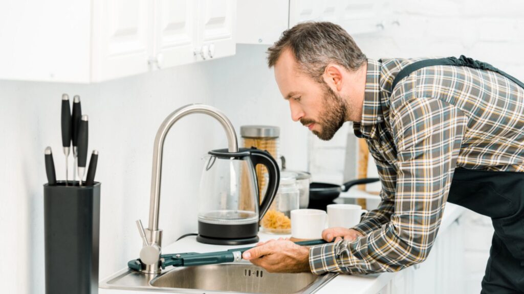 góc nhìn bên của thợ sửa ống nước đang sửa vòi bằng mỏ lết trong bếp