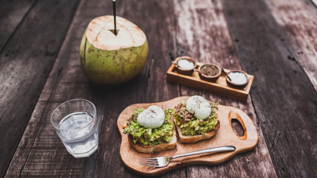 Tasty organic healthy breakfast - poached eggs on toast with avocado, water with lime, young coconut