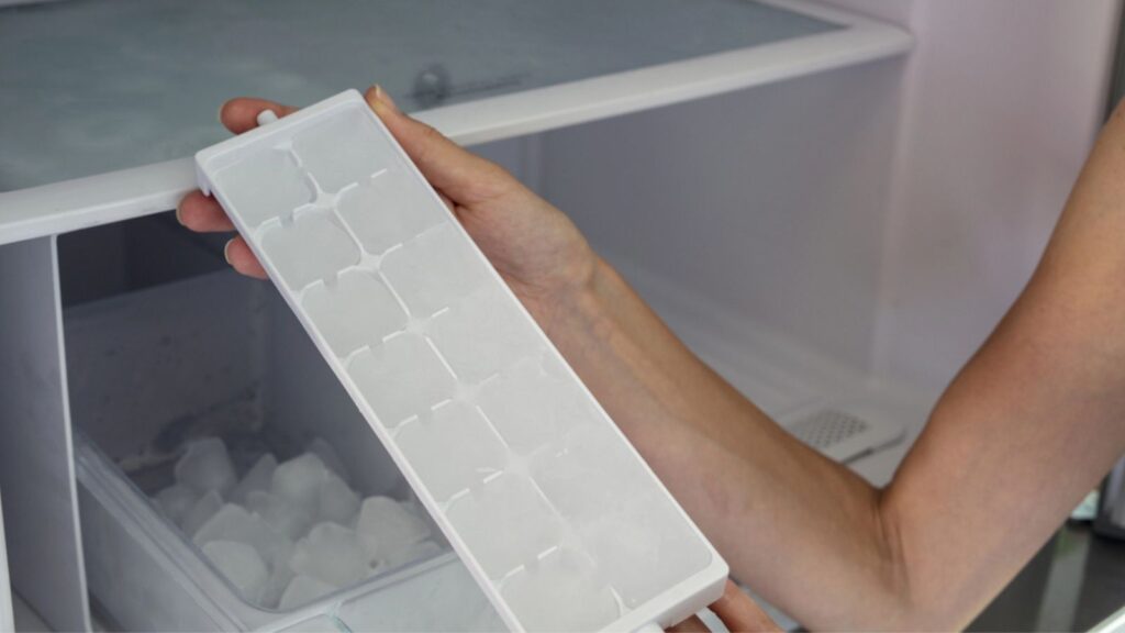 Woman hands taking ice cubes from fridge close up