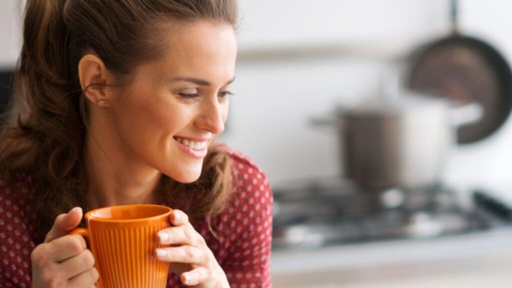 Woman smiling in kitchen holding mug