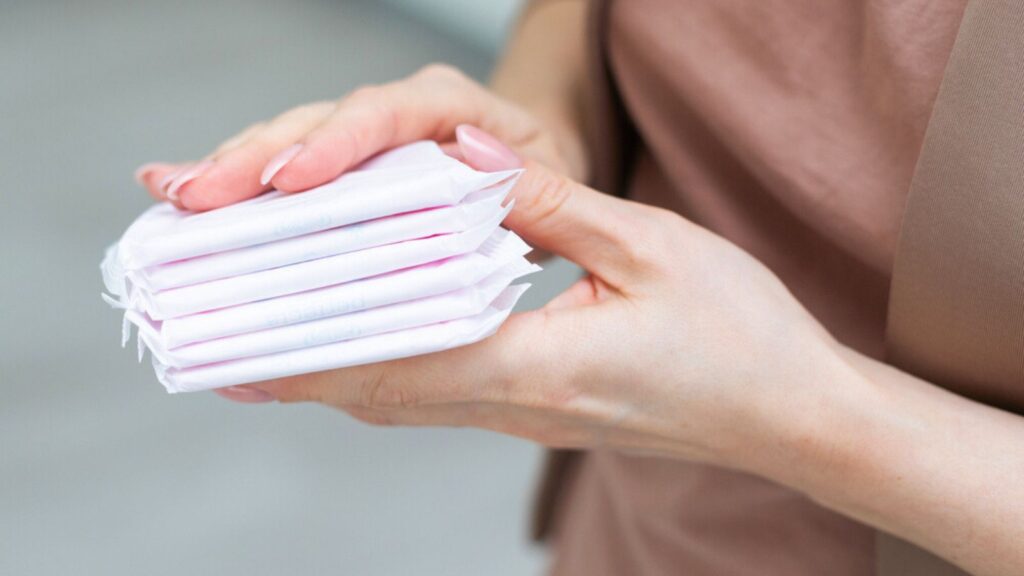 Young adult woman hand holding packs of sanitary towel on light background. Pastel color. Closeup. Empty place for text. High quality photo