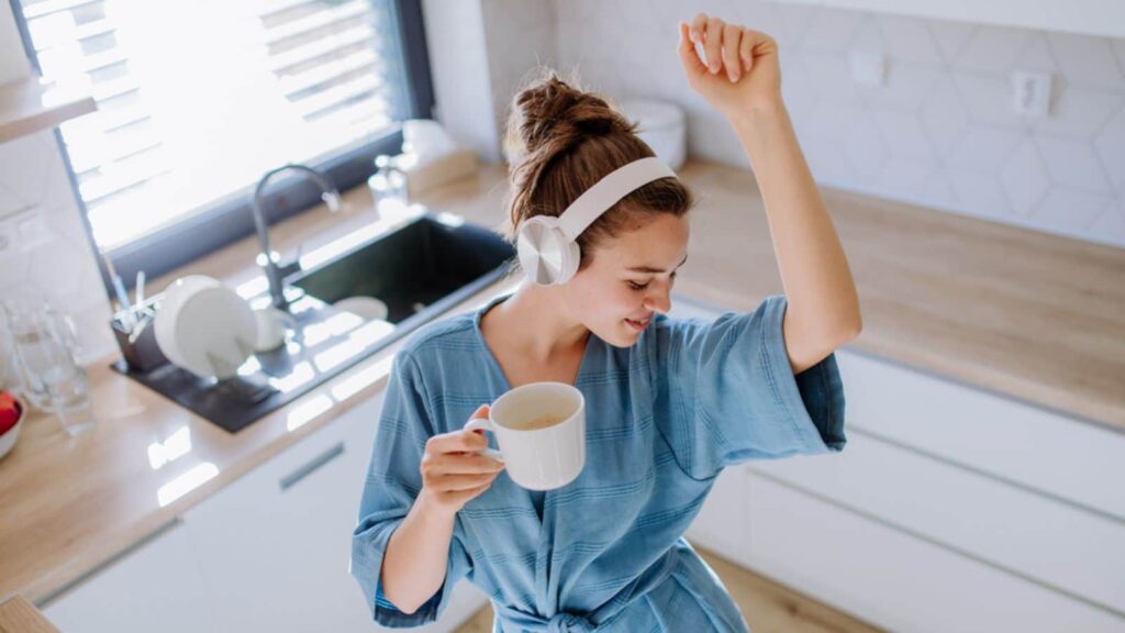 Young woman enjoying cup of coffee and listening music and dancing at morning