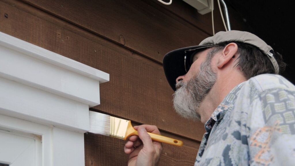 senior man painting the doorway with white paint