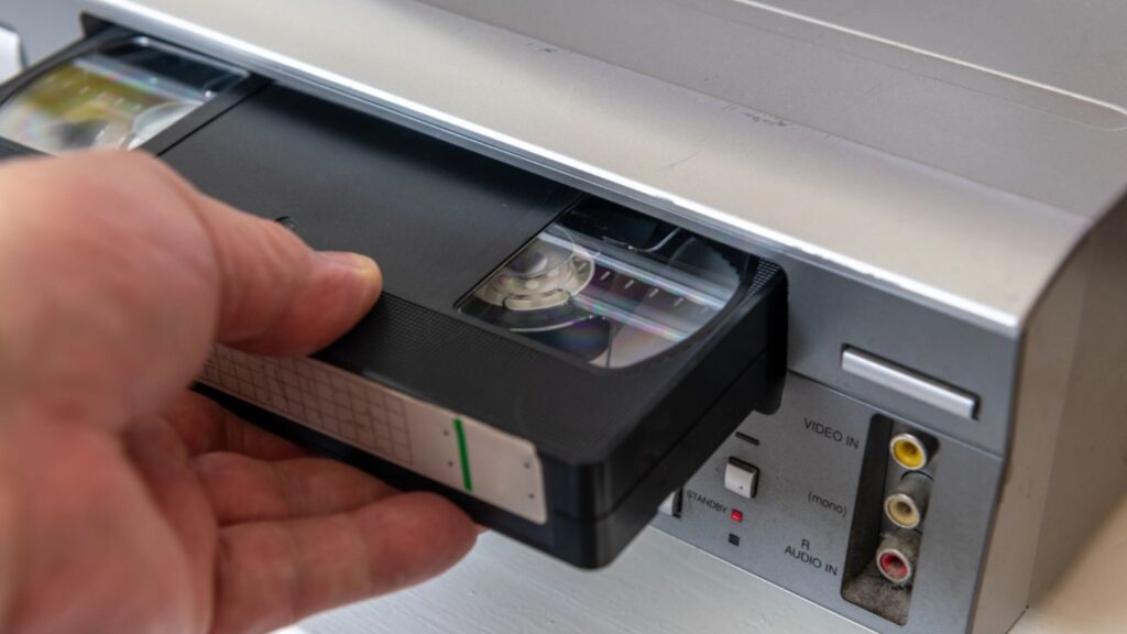 A person inserting a video cassette into a vintage video player.