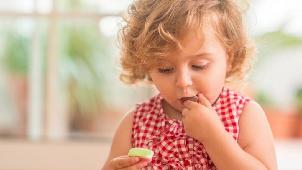 Beautiful blonde child with blue eyes eating candy at home