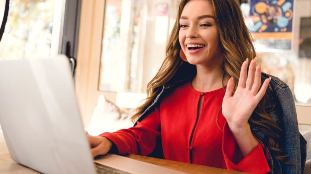 Cheerful blogger waving hand while having video call on laptop