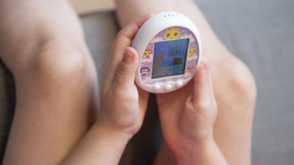 Child hand gently cradle Tamagotchi toy, evoking nostalgia for popular virtual pet craze 1990s, developing empathy, Nurturing childhood memories, Frankfurt