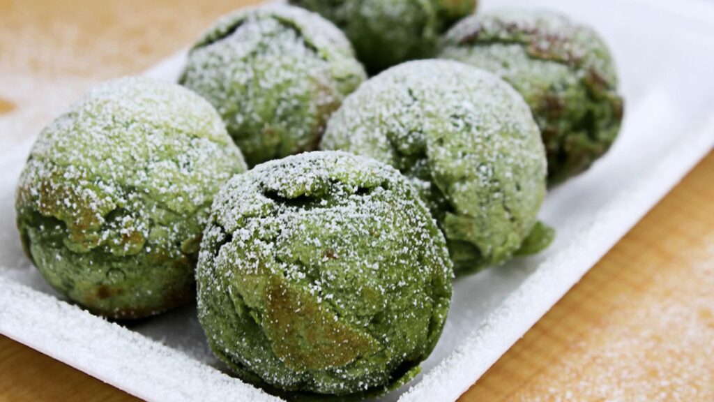 Green sweet candy balls made from matcha tea on a white platter sprinkled with powdered sugar.