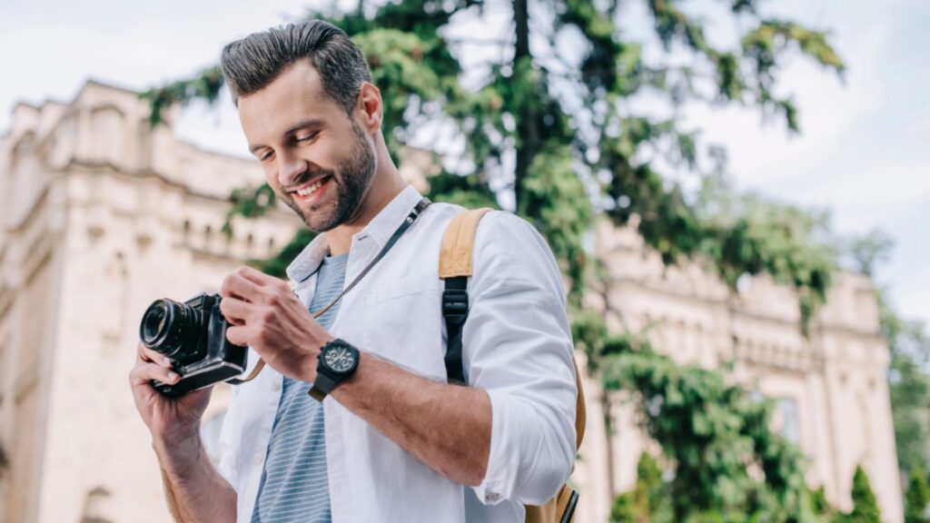 Low angle view of cheerful bearded man holding digital camera