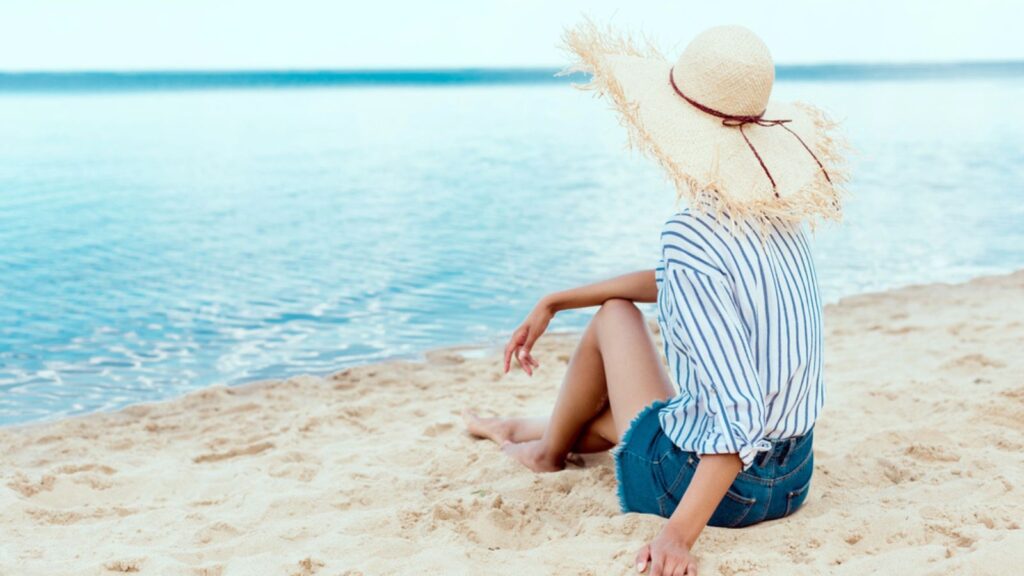 Rear view of young woman in straw hat relaxing on sandy beach